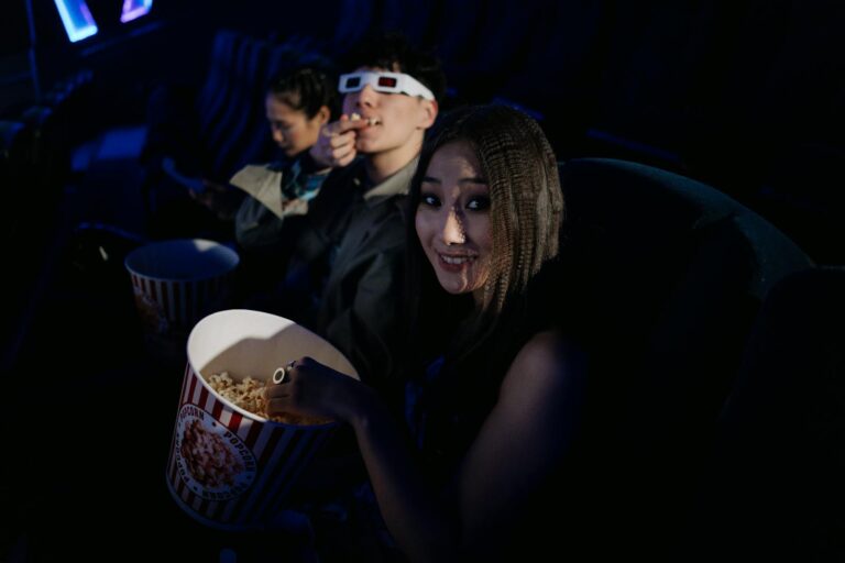 Group of friends wearing 3D glasses and enjoying popcorn at a movie theater.