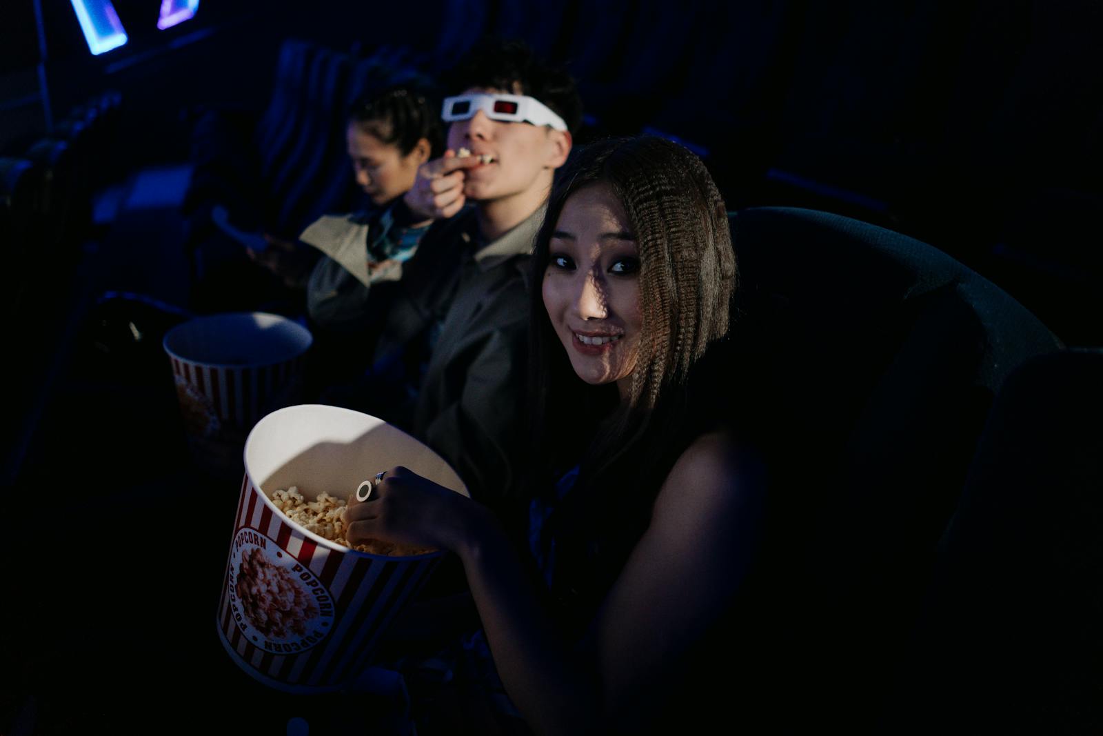 Group of friends wearing 3D glasses and enjoying popcorn at a movie theater.