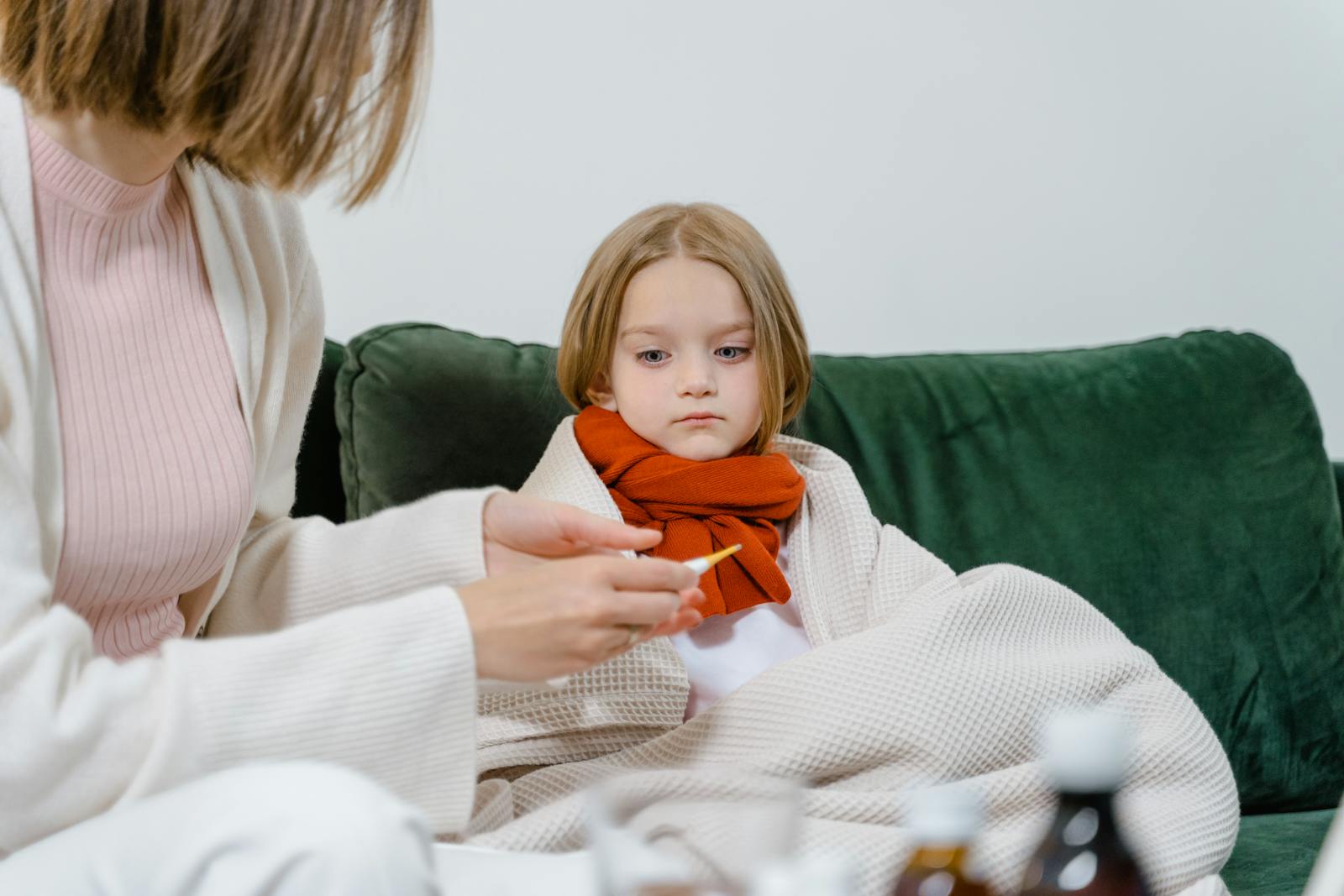A caring moment of a woman checking a sick child's temperature on a cozy green couch indoors.