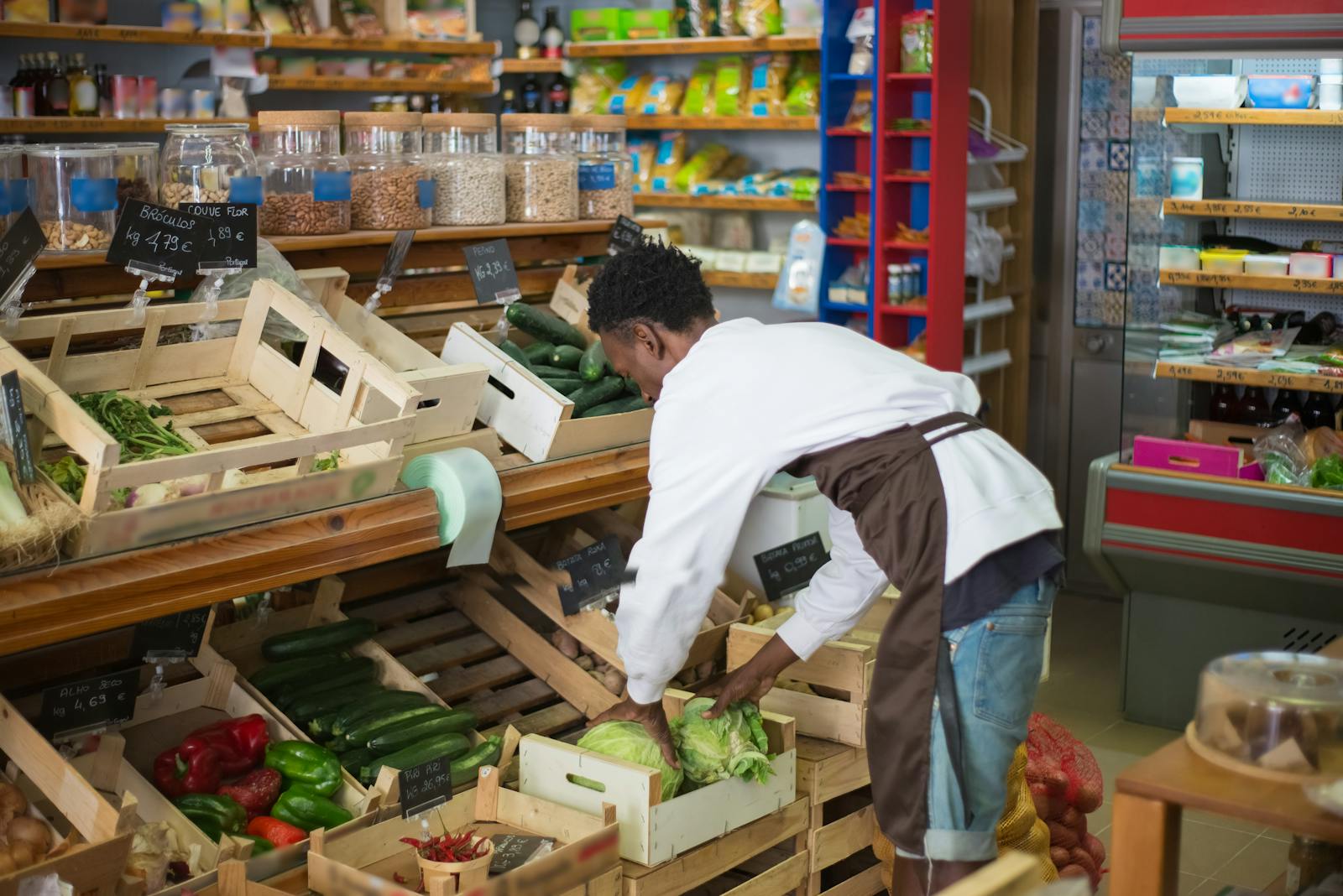 Grocery store worker arranging fresh vegetables in a market display.