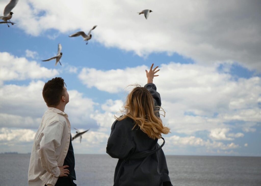 A young couple by the sea watching seagulls in a cloudy sky. Captured in Saint Petersburg.