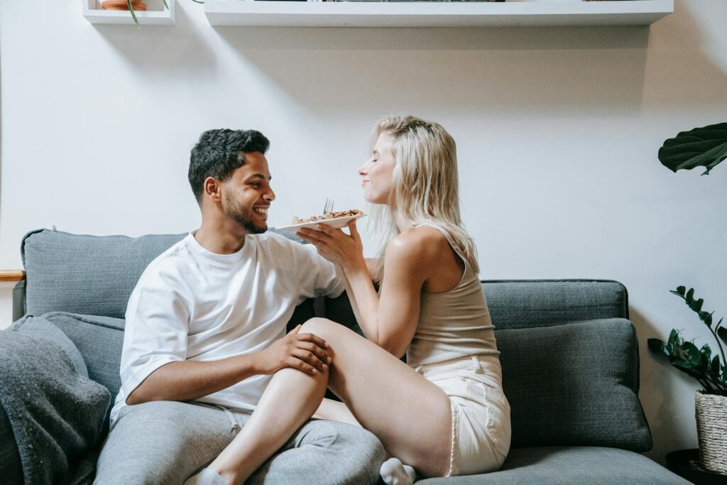 Romantic moment of a couple sharing food on a cozy couch at home.