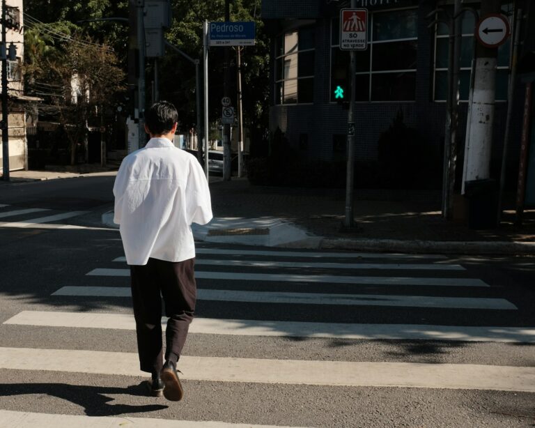 a man in a white shirt is crossing the street