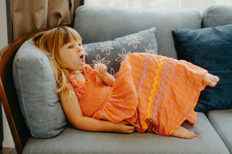 Young girl in orange dress lying on sofa.