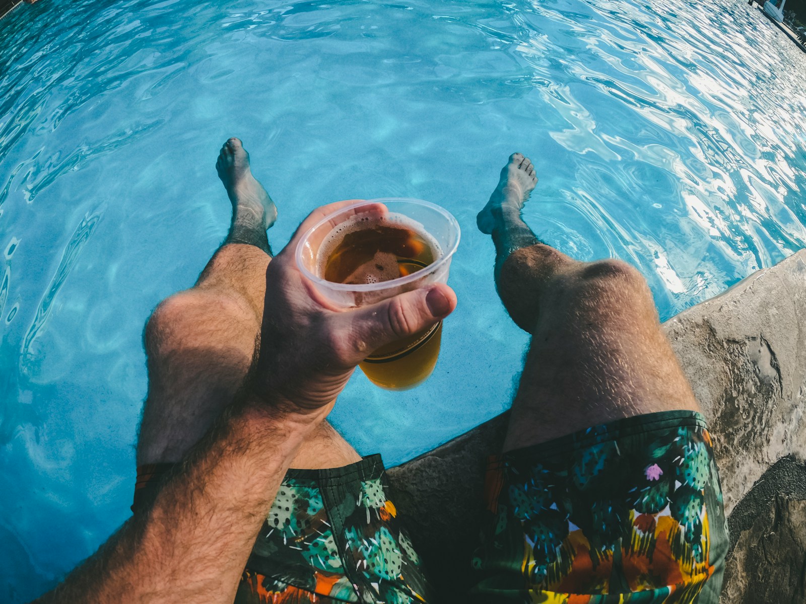 man holding a cup of drink while dipped in the swimming pool