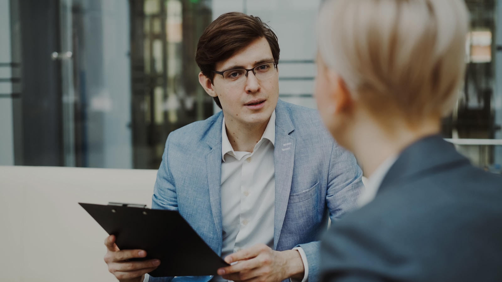 Man in suit holding clipboard talking to woman