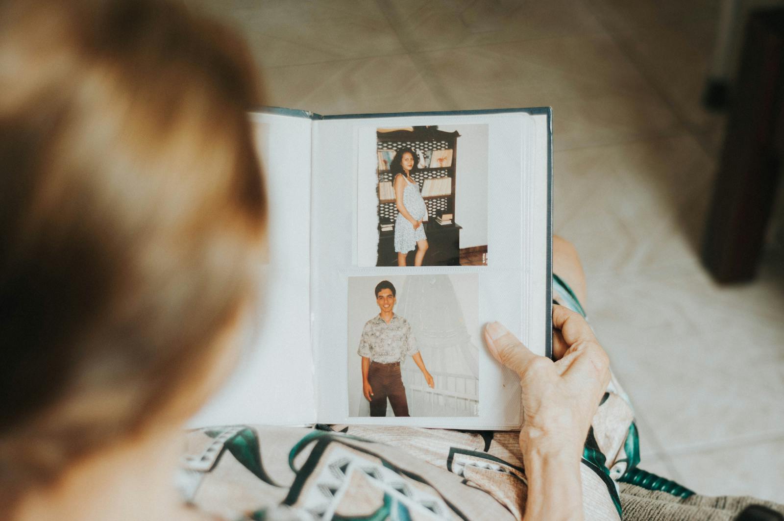 A senior woman reminisces while looking at a photo album indoors.