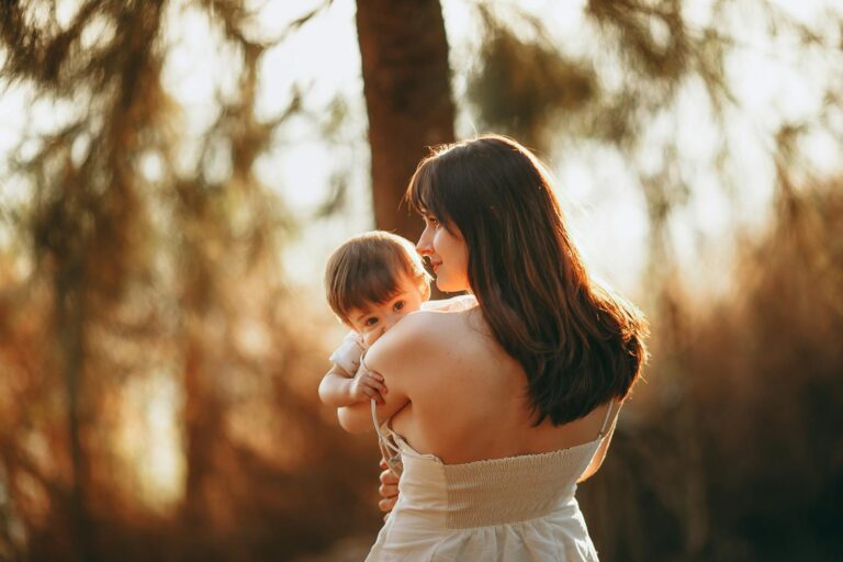 A mother gently holds her child in a serene outdoor setting during sunset.