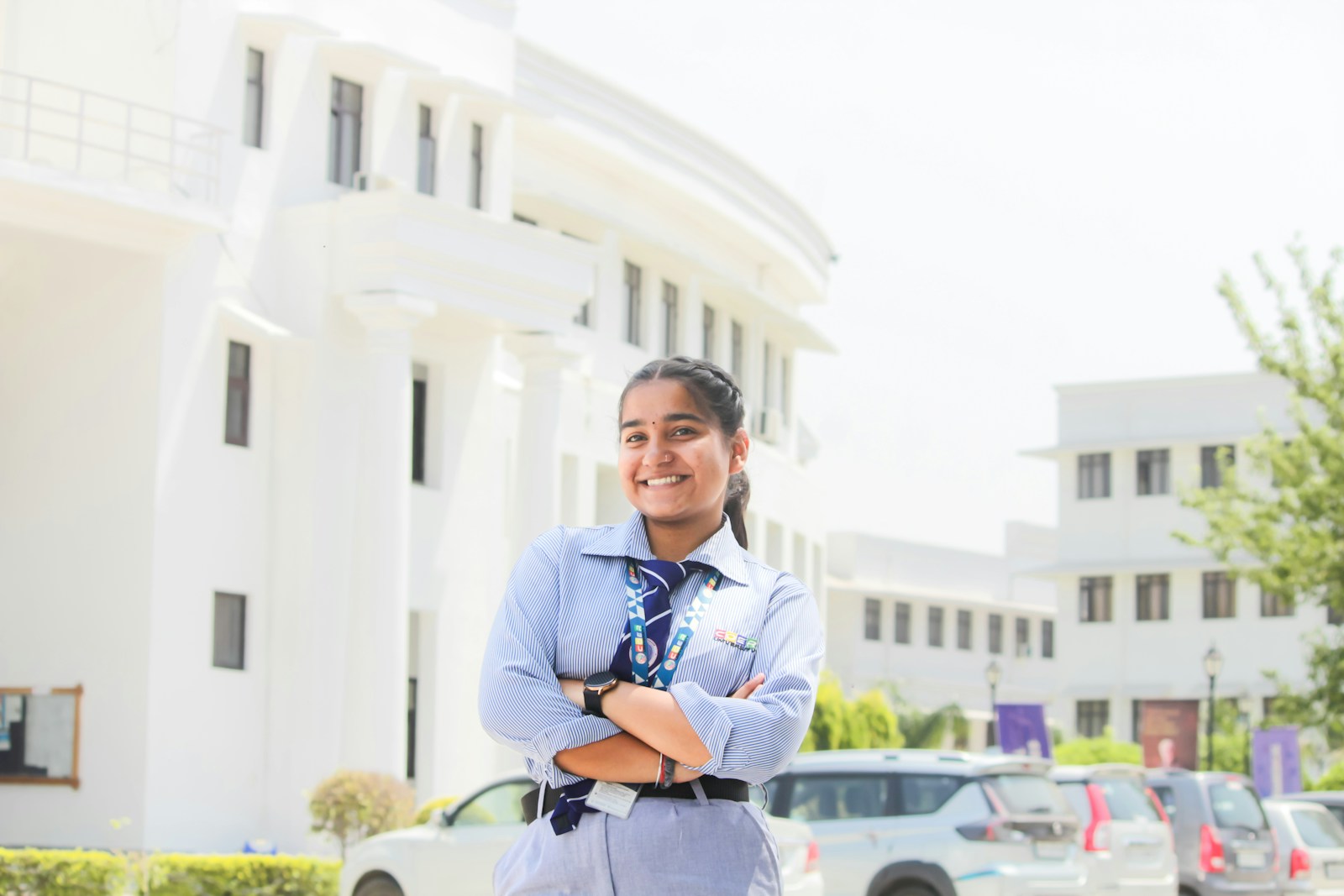 A smiling girl in school uniform stands outside a building.
