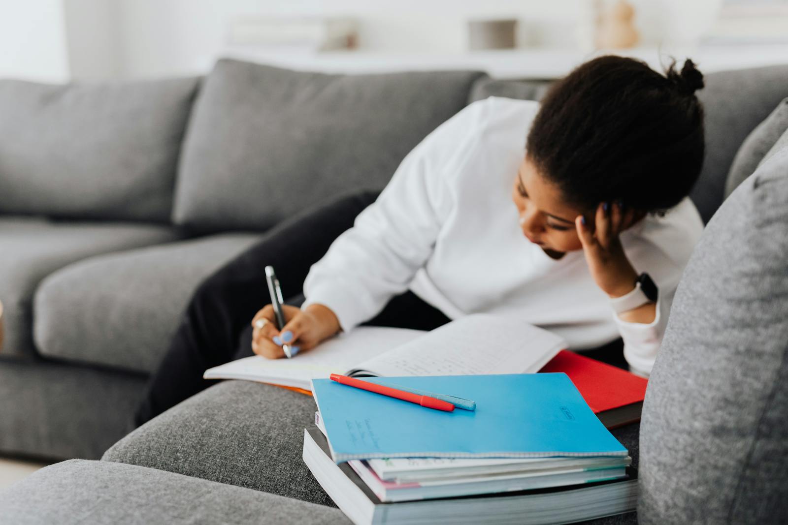 An adult woman focused on studying and writing, surrounded by books in a cozy indoor setting.