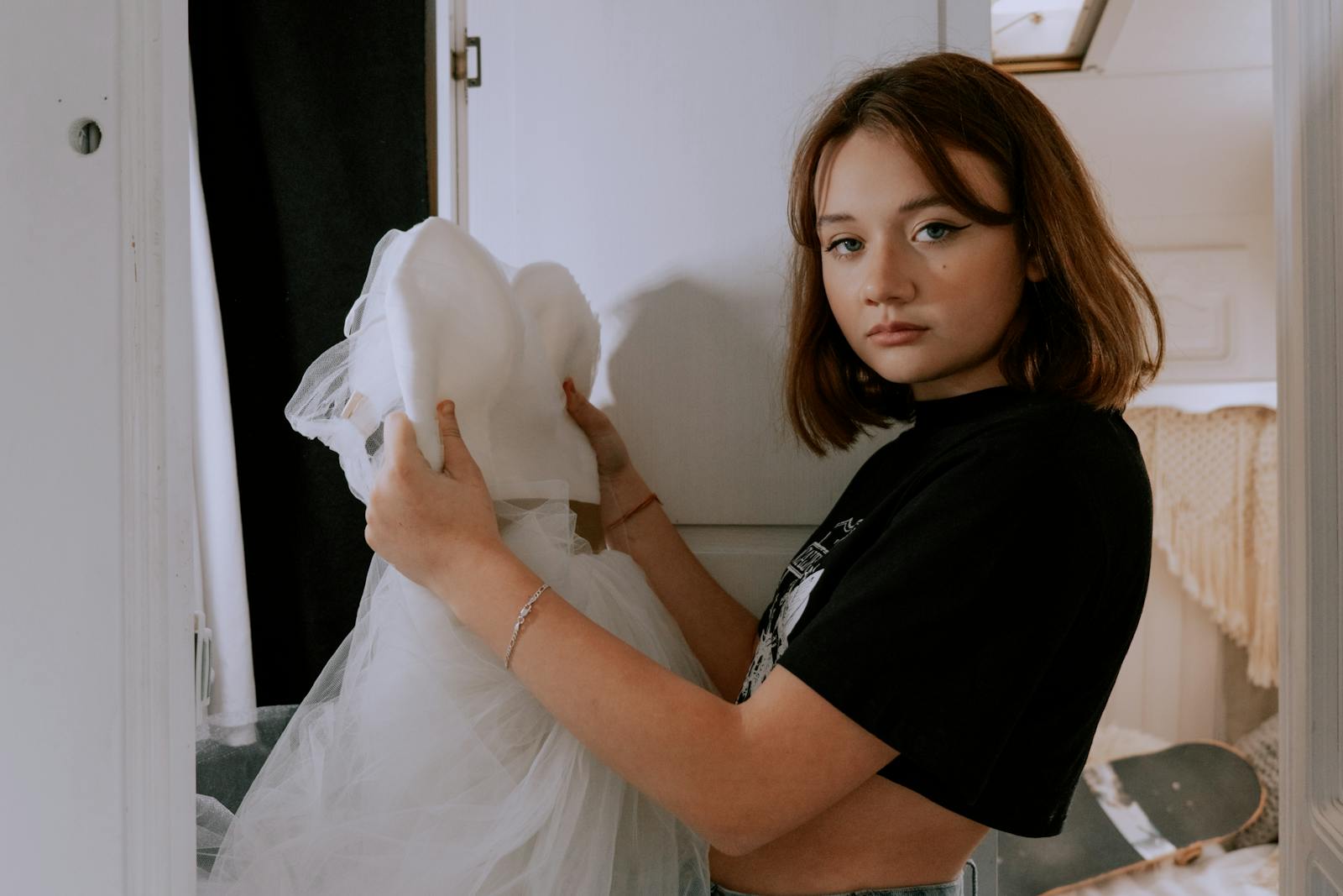 Teen girl holding a wedding dress indoors, conveying contemplation and future planning.