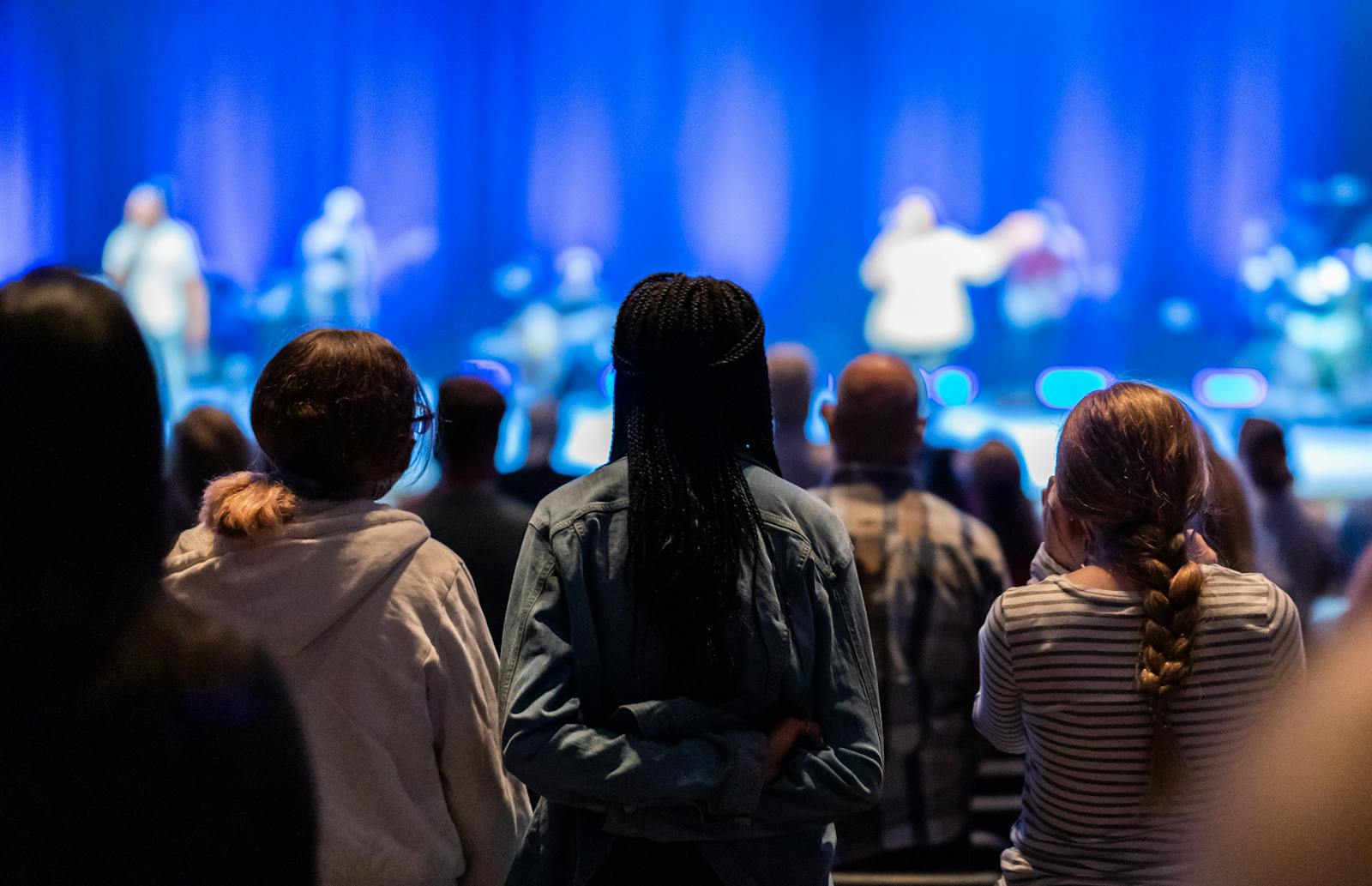 Back view of unrecognizable people looking at stage during performance in concert hall with shining lamps