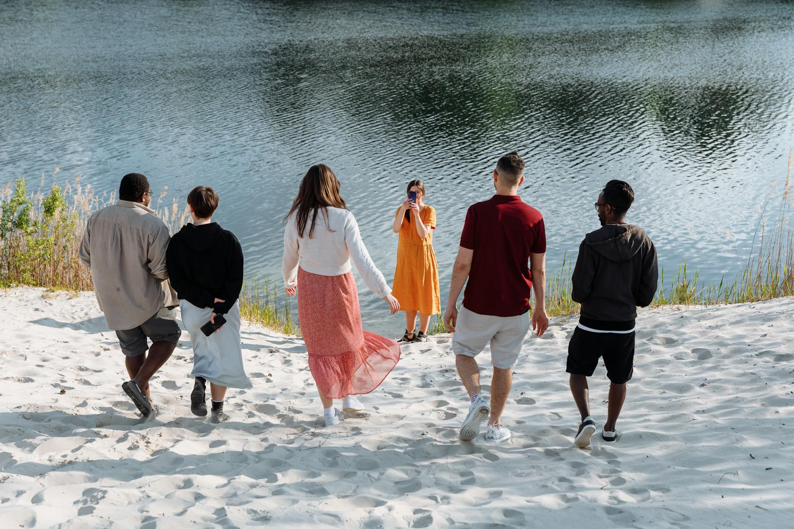 A group of friends enjoy a sunny day near a calm lake, capturing memories on a sandy beach.