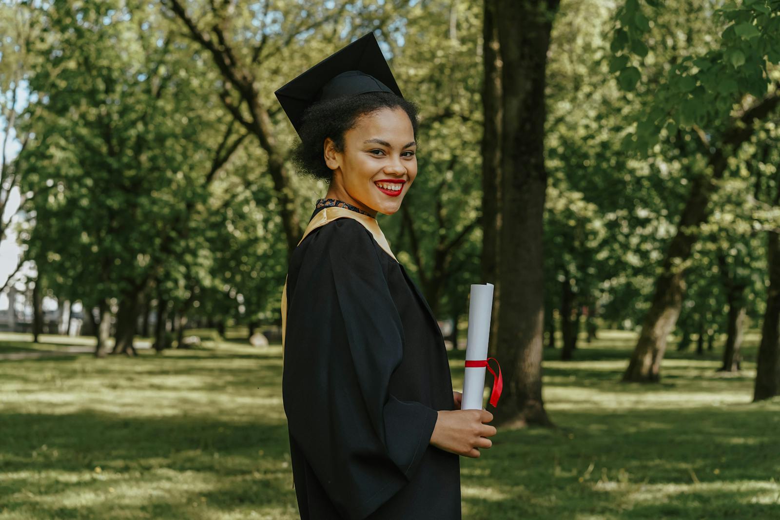 Smiling graduate holding diploma in a park setting