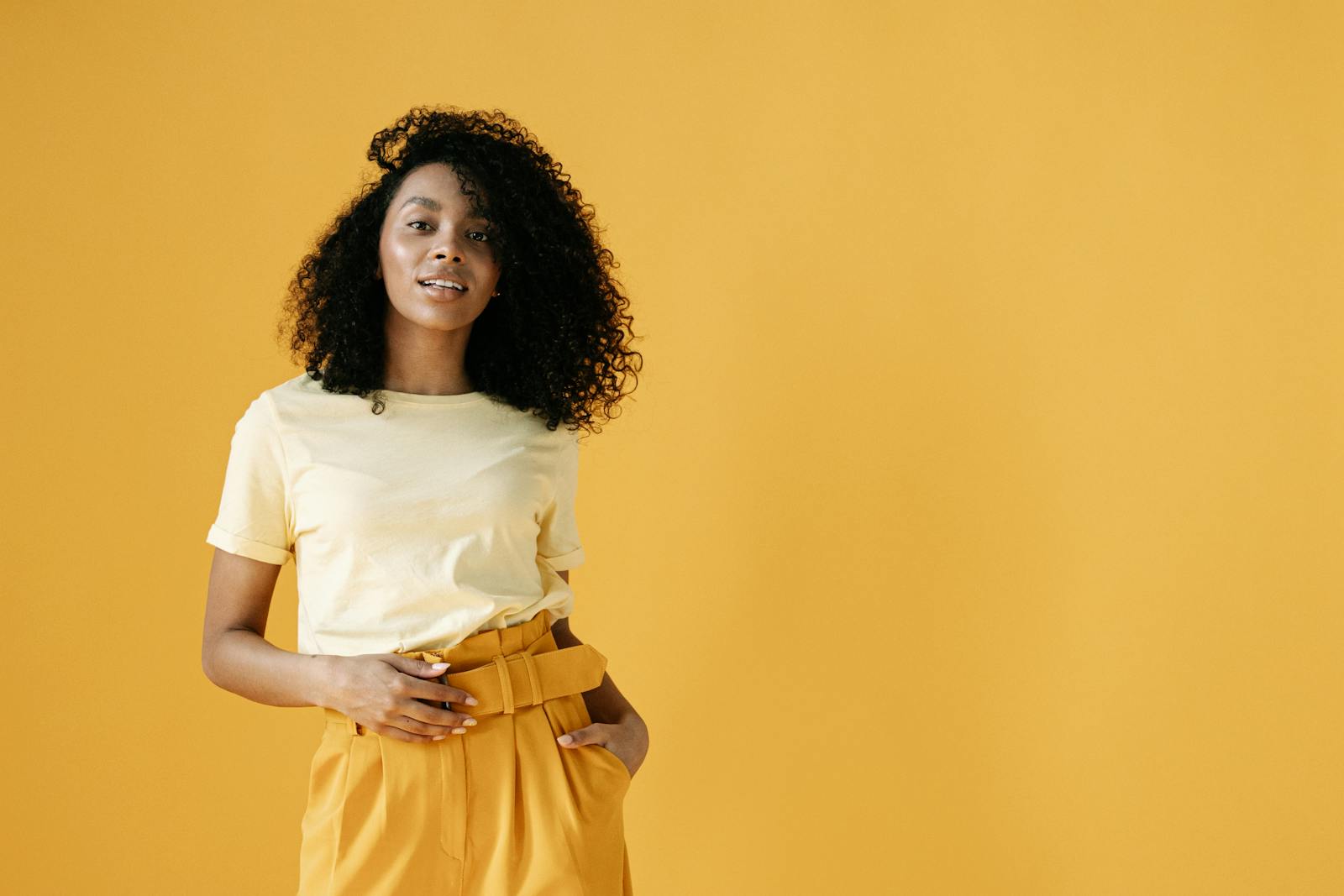 Stylish young woman in yellow fashion standing confidently against a vibrant backdrop.