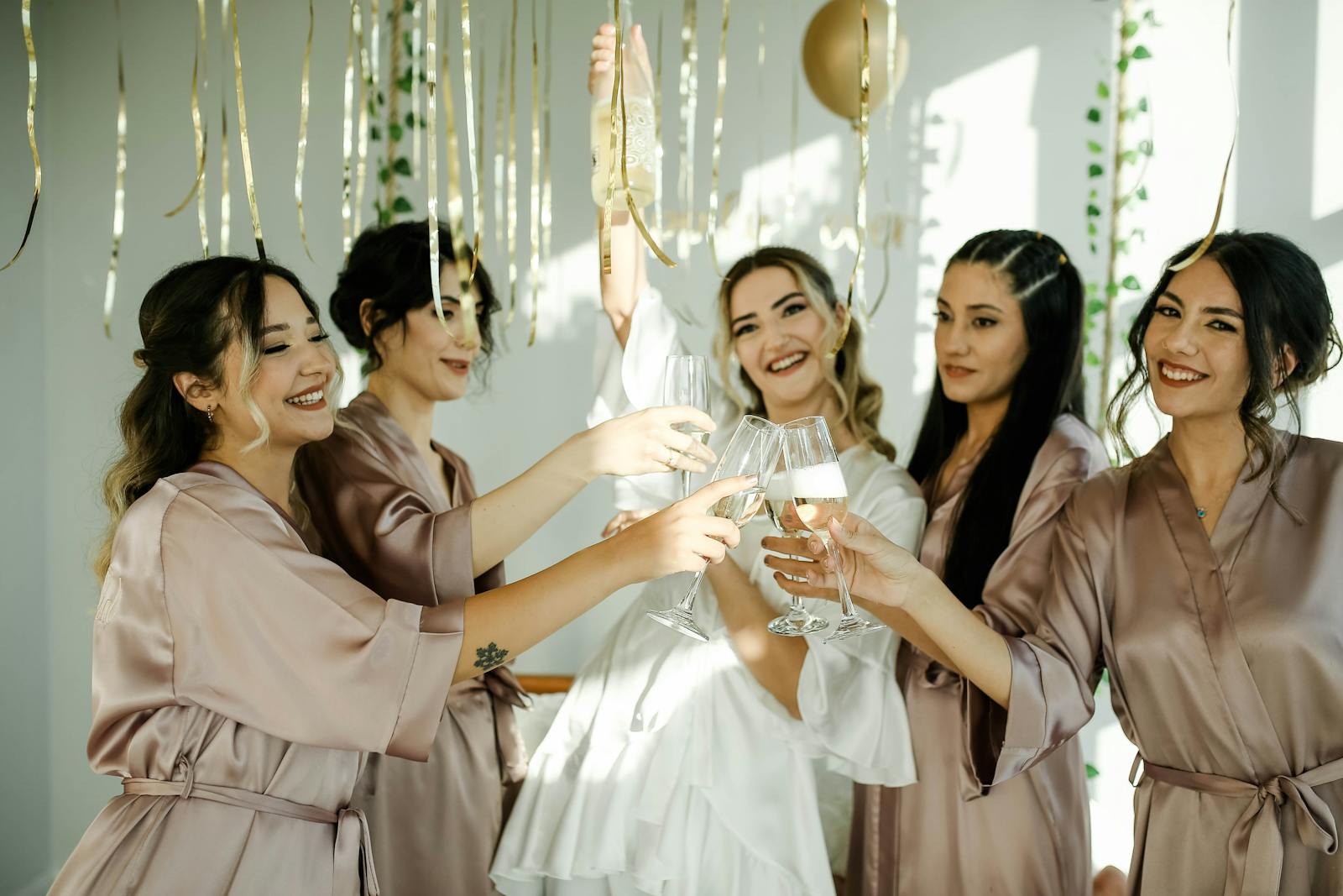 Group of women celebrating a bachelorette party with champagne in stylish robes.