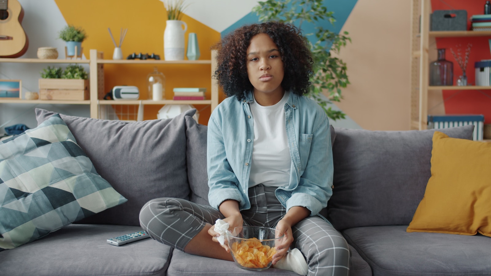 Young woman watching TV with snacks on couch.