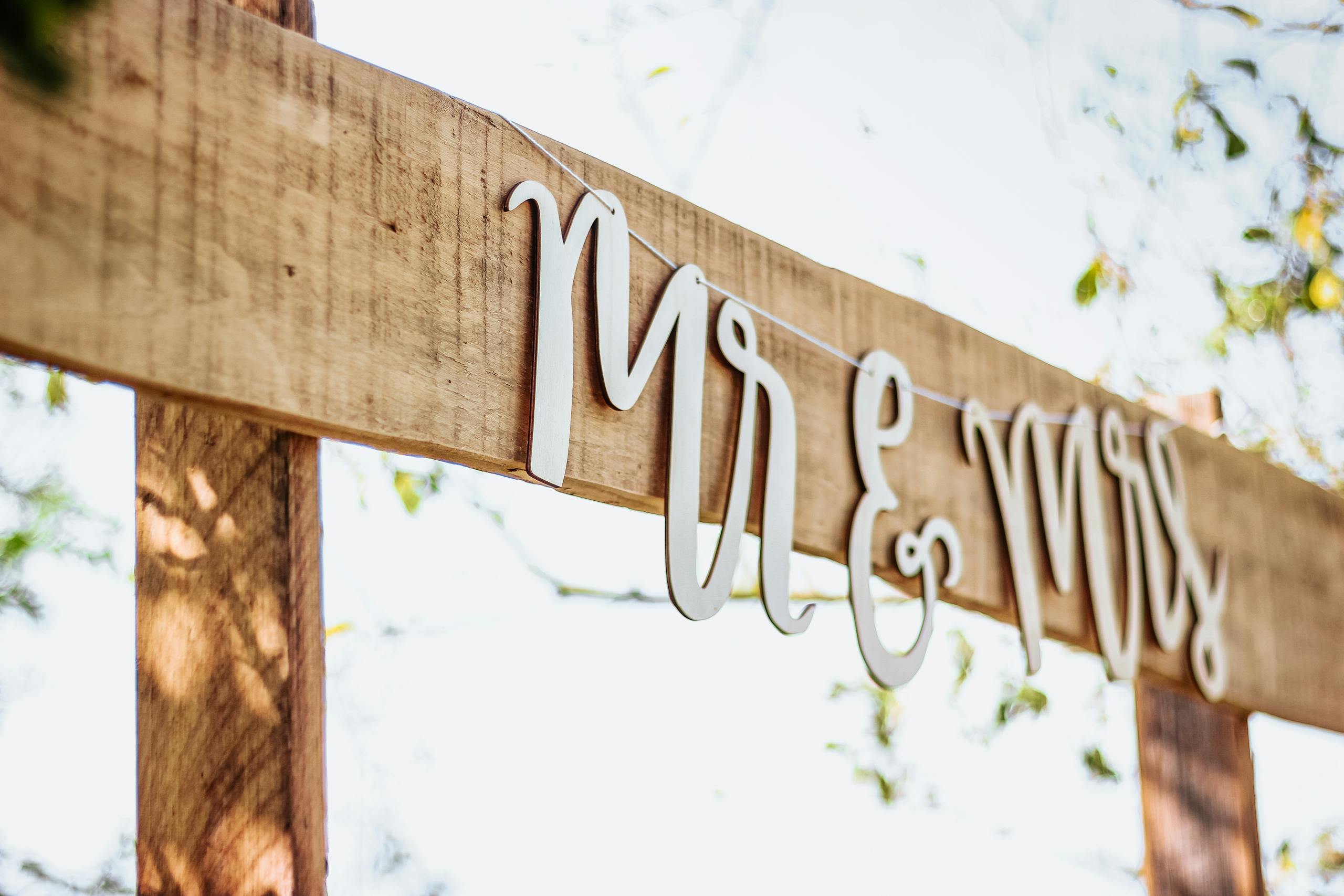 A close-up of a rustic wooden wedding sign featuring 'Mr & Mrs' text on a sunny day.