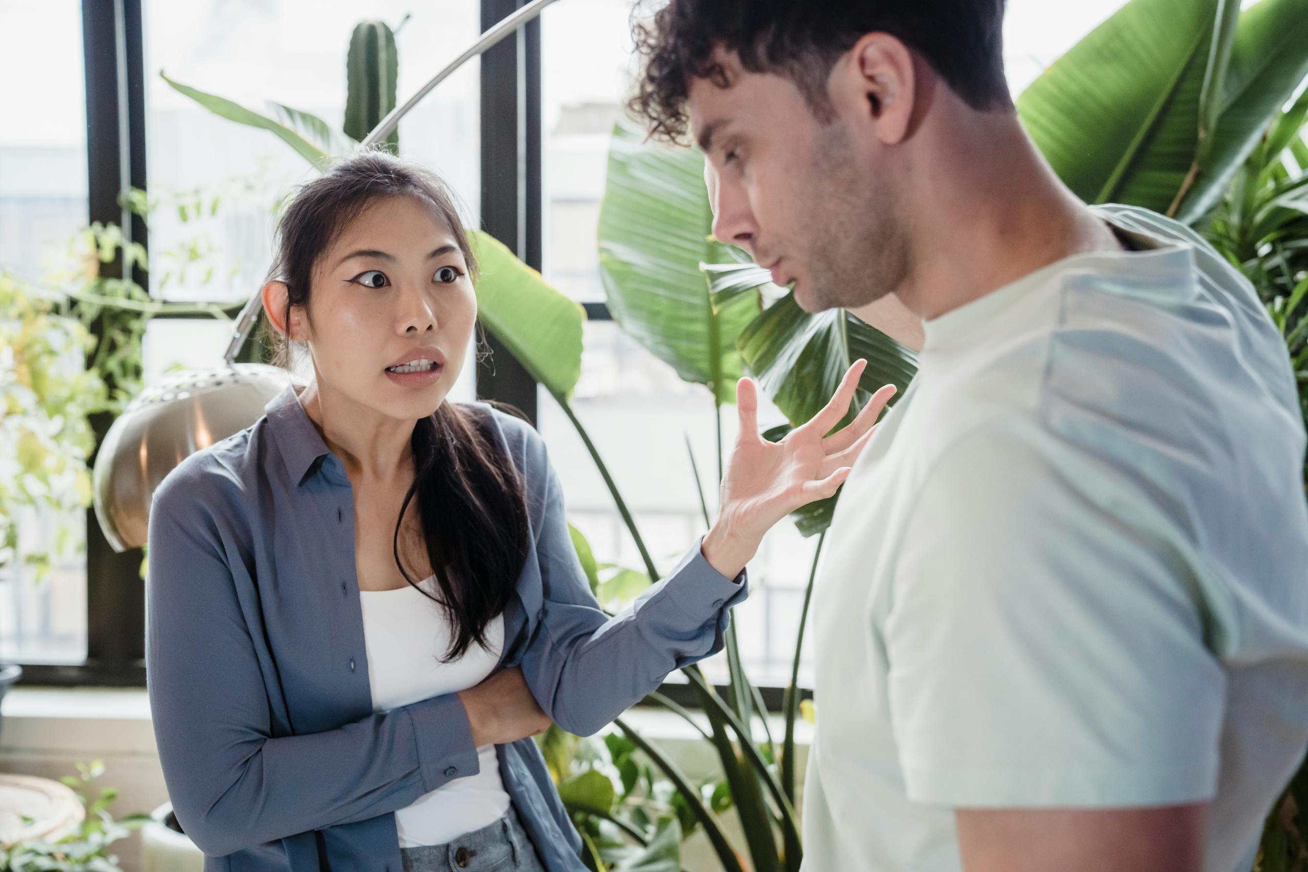 A couple engaged in a heated discussion indoors surrounded by plants, expressing emotions.
