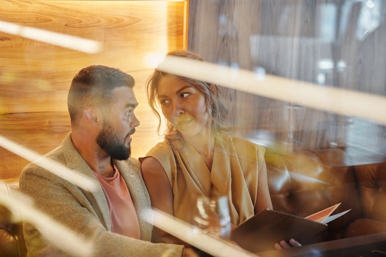 A couple enjoys a warm conversation in a cozy restaurant, viewed through a glass panel.