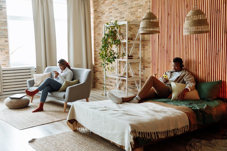 A couple relaxing with gadgets in a stylish loft bedroom with natural decor.