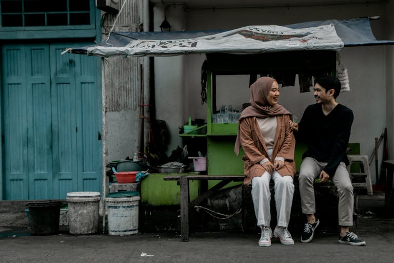 A couple sits and chats at a street food stall, enjoying a casual moment together.