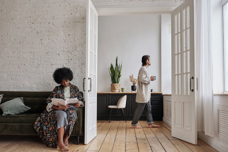 A cozy home scene with a woman reading and a man enjoying coffee on a sunny morning.