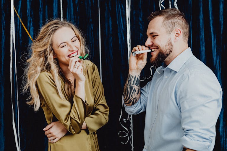 A joyful couple laughing and celebrating indoors with party favors and streamers.