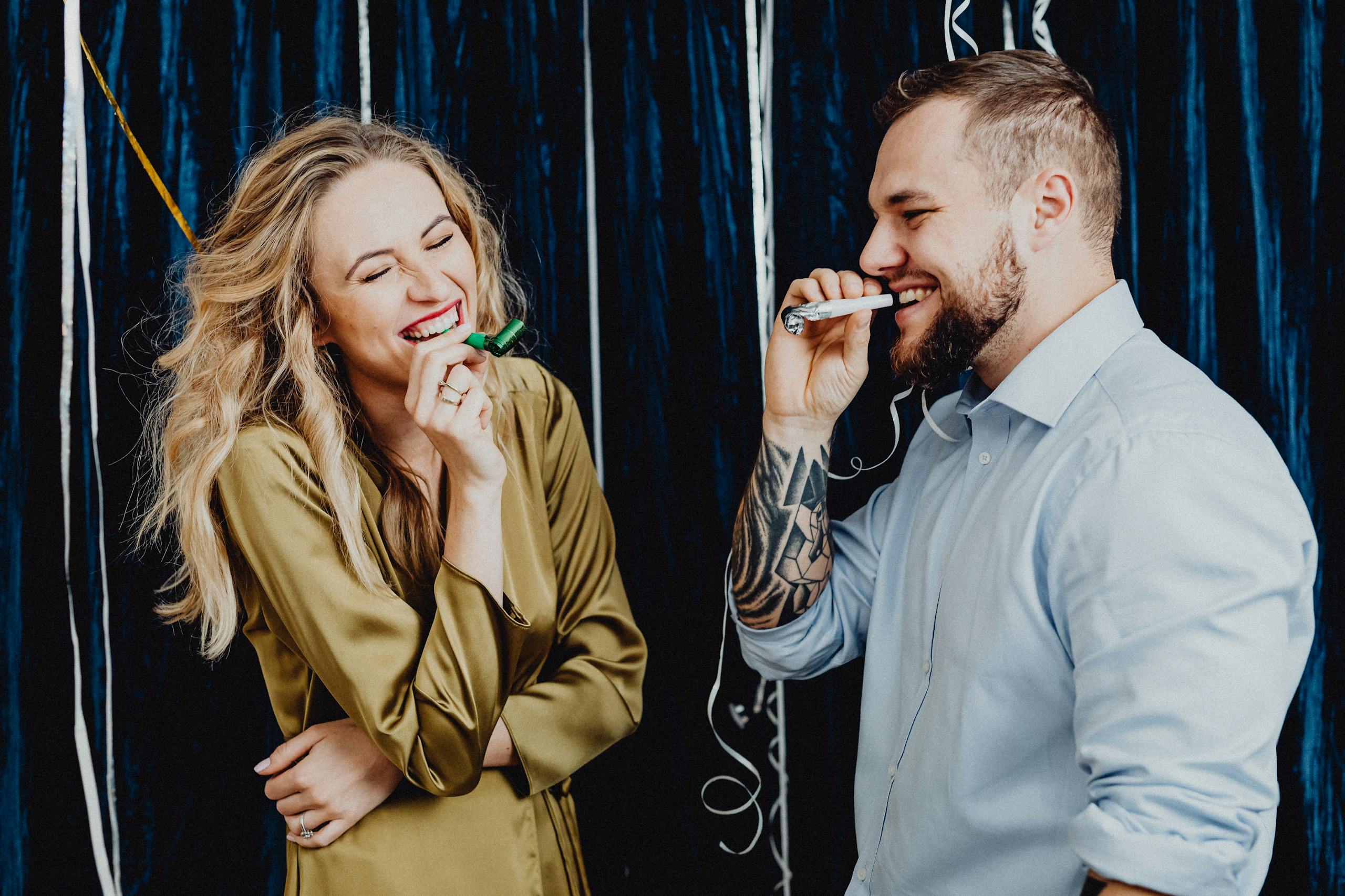 A joyful couple laughing and celebrating indoors with party favors and streamers.