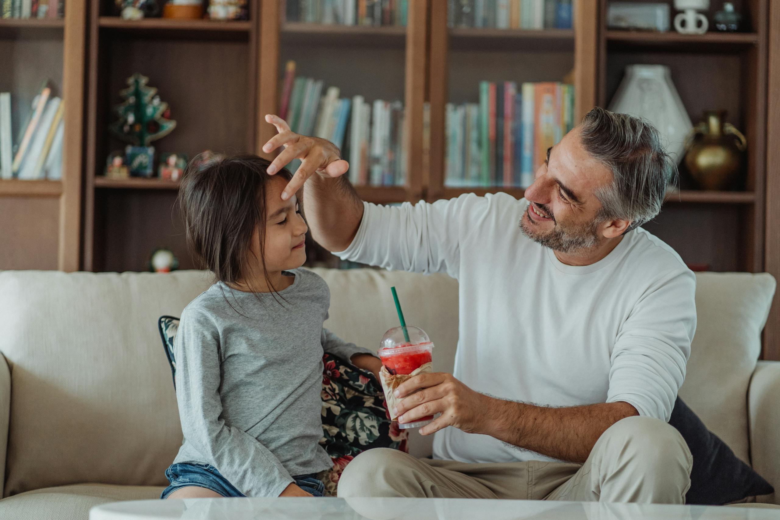 A joyful father bonding with his daughter sharing a smoothie at home.