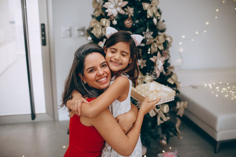 A joyful mother and daughter embrace in front of a decorated Christmas tree, sharing love and festive cheer.