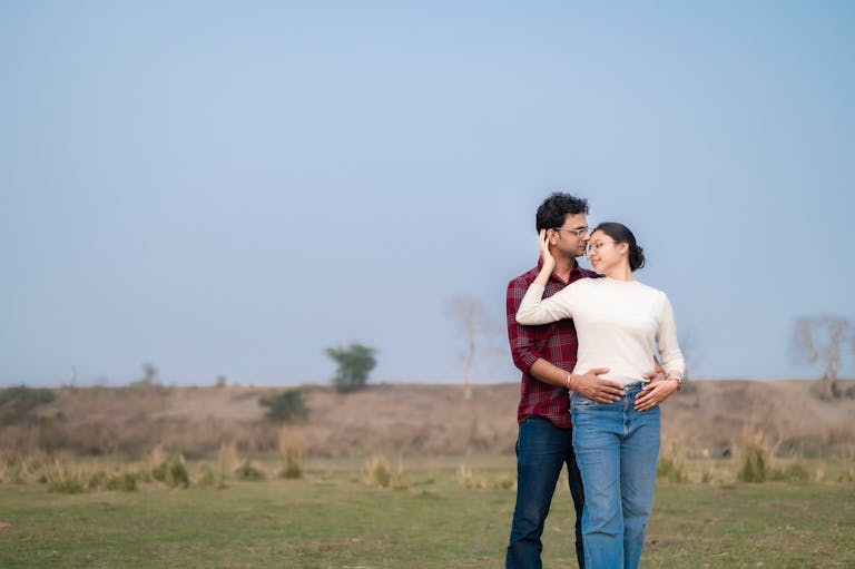 A loving couple embraces in a picturesque outdoor meadow, enjoying a serene moment together.