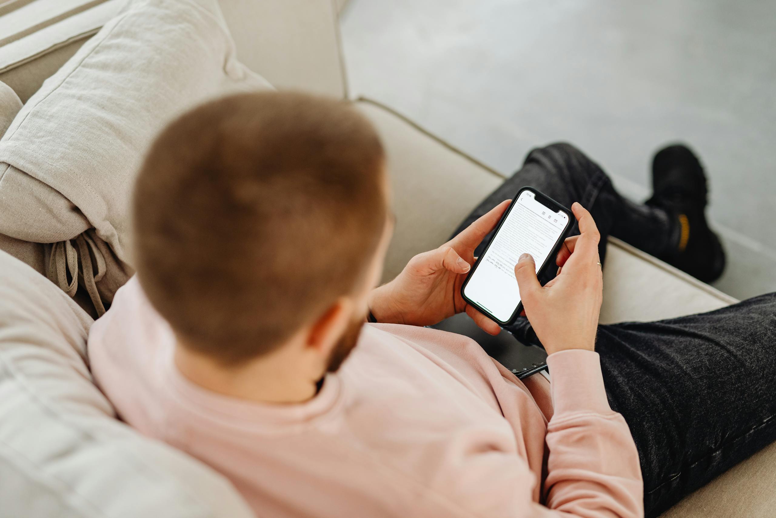 A man sitting on a sofa, engaged with a smartphone, enjoying leisure time indoors.