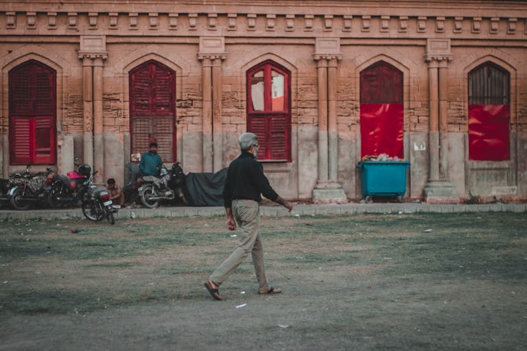 A man walks past a historic building with red windows, capturing urban life in a cityscape.