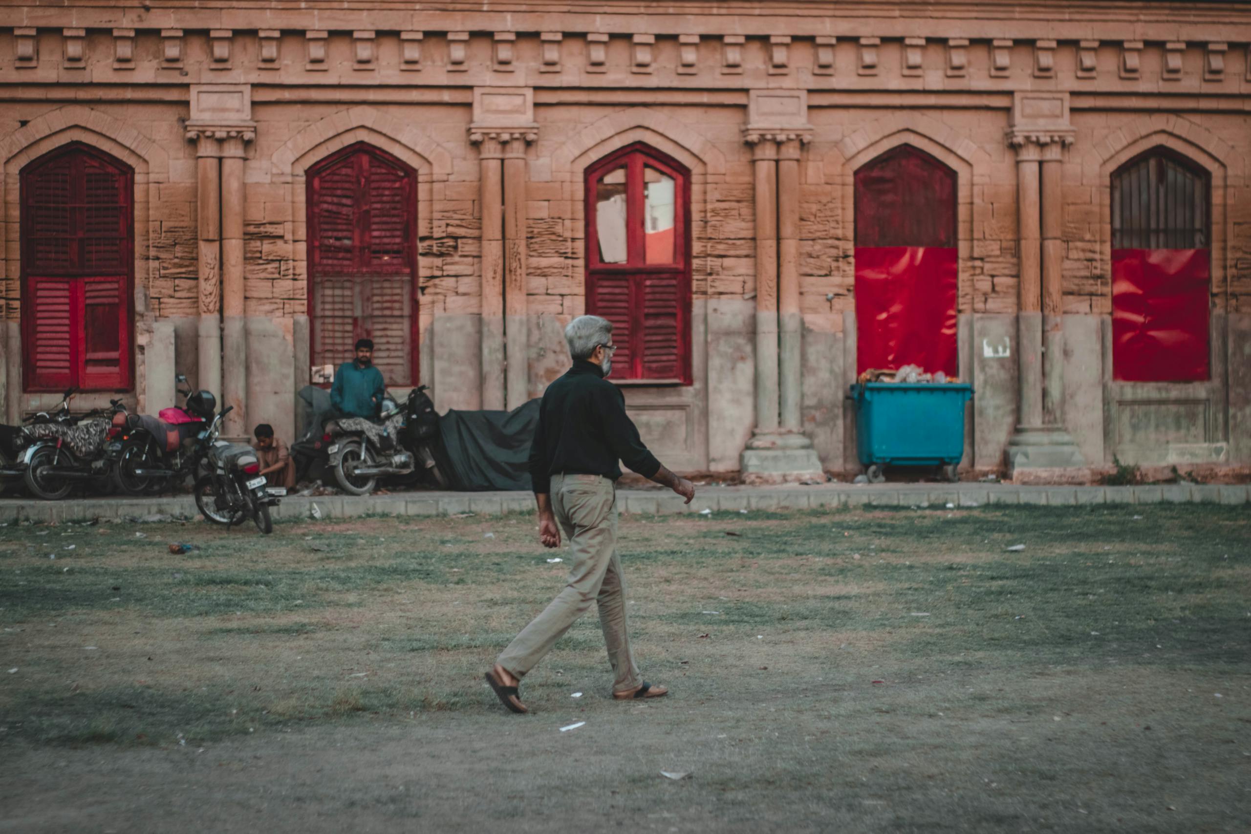 A man walks past a historic building with red windows, capturing urban life in a cityscape.