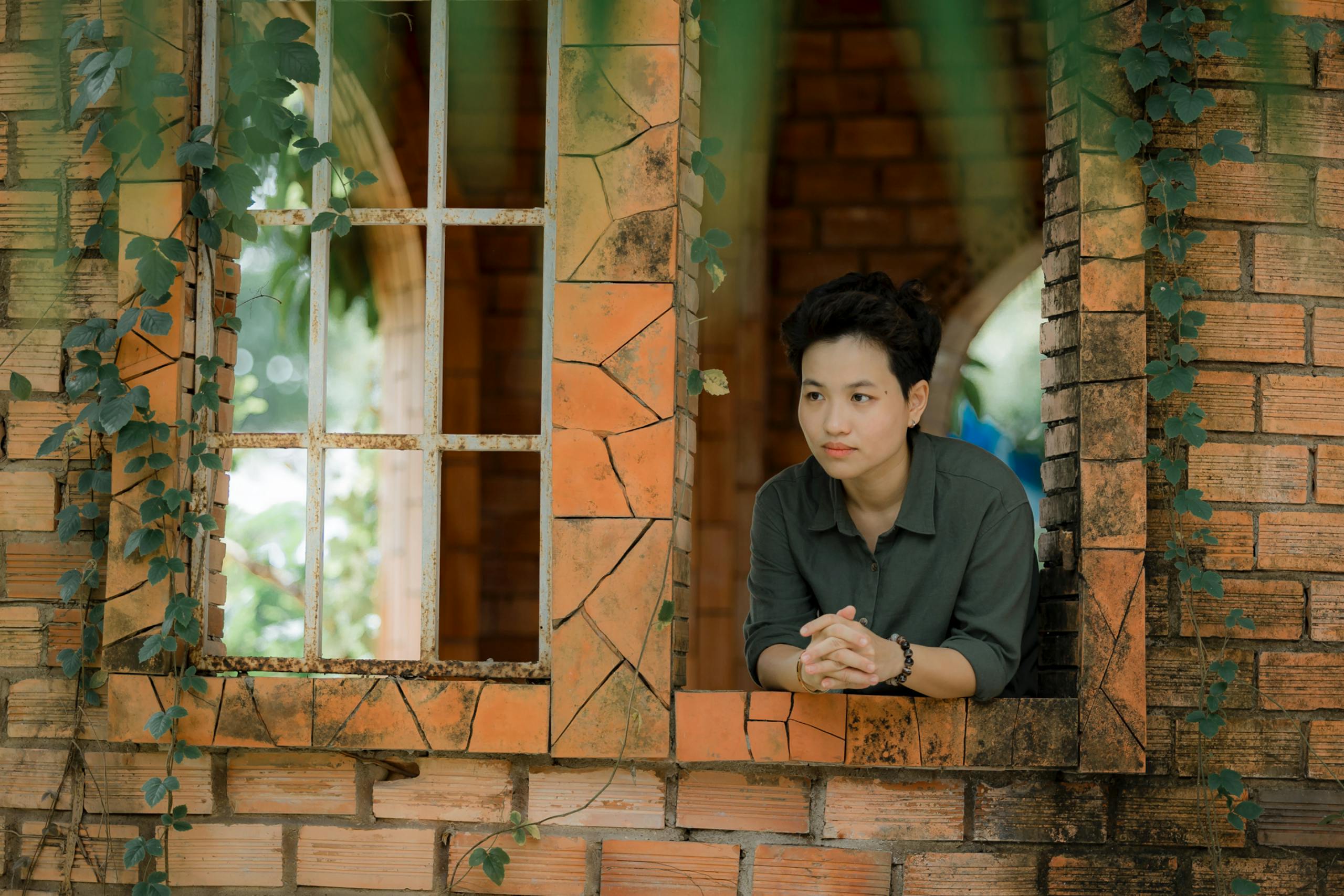 A person leans on a rustic brick window surrounded by greenery, lost in thought.
