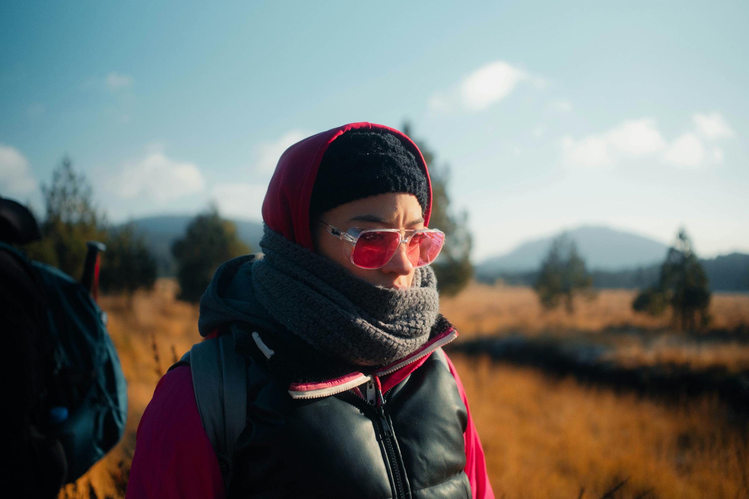 A person warmly dressed with pink sunglasses enjoying an autumn hike.