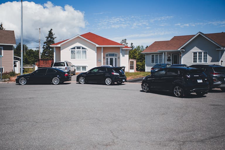 A quiet suburban street with parked cars in front of modern houses under a clear blue sky.