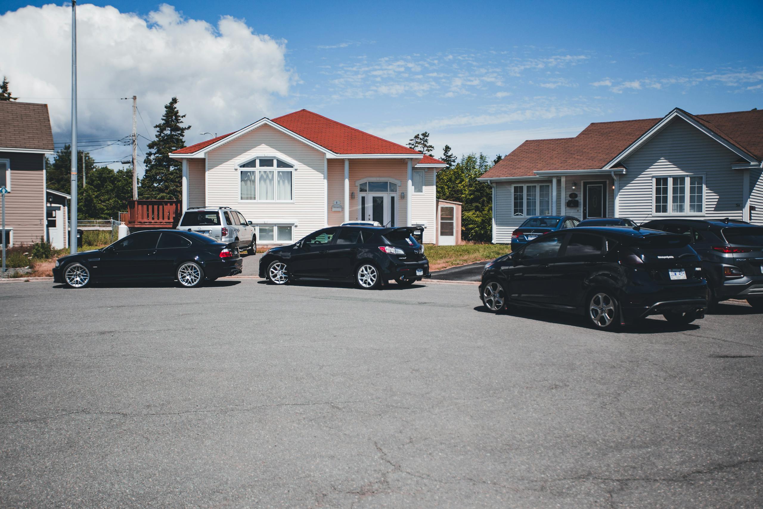 A quiet suburban street with parked cars in front of modern houses under a clear blue sky.
