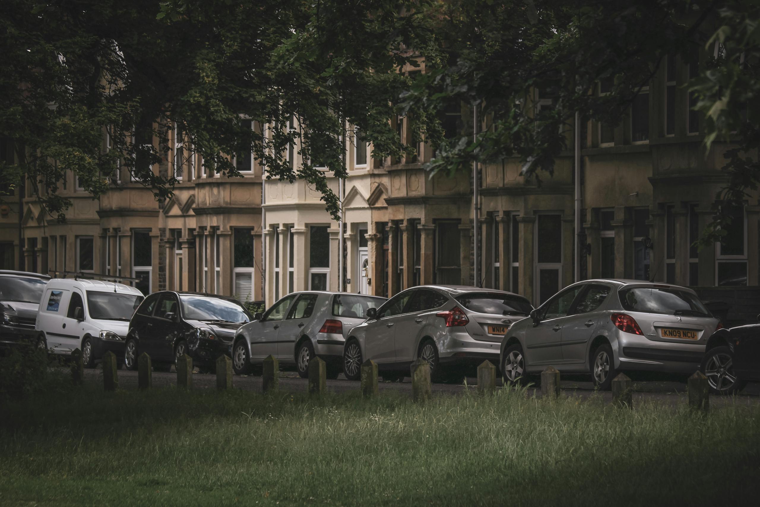 A row of parked cars along a tree-lined residential street in Bristol, England.