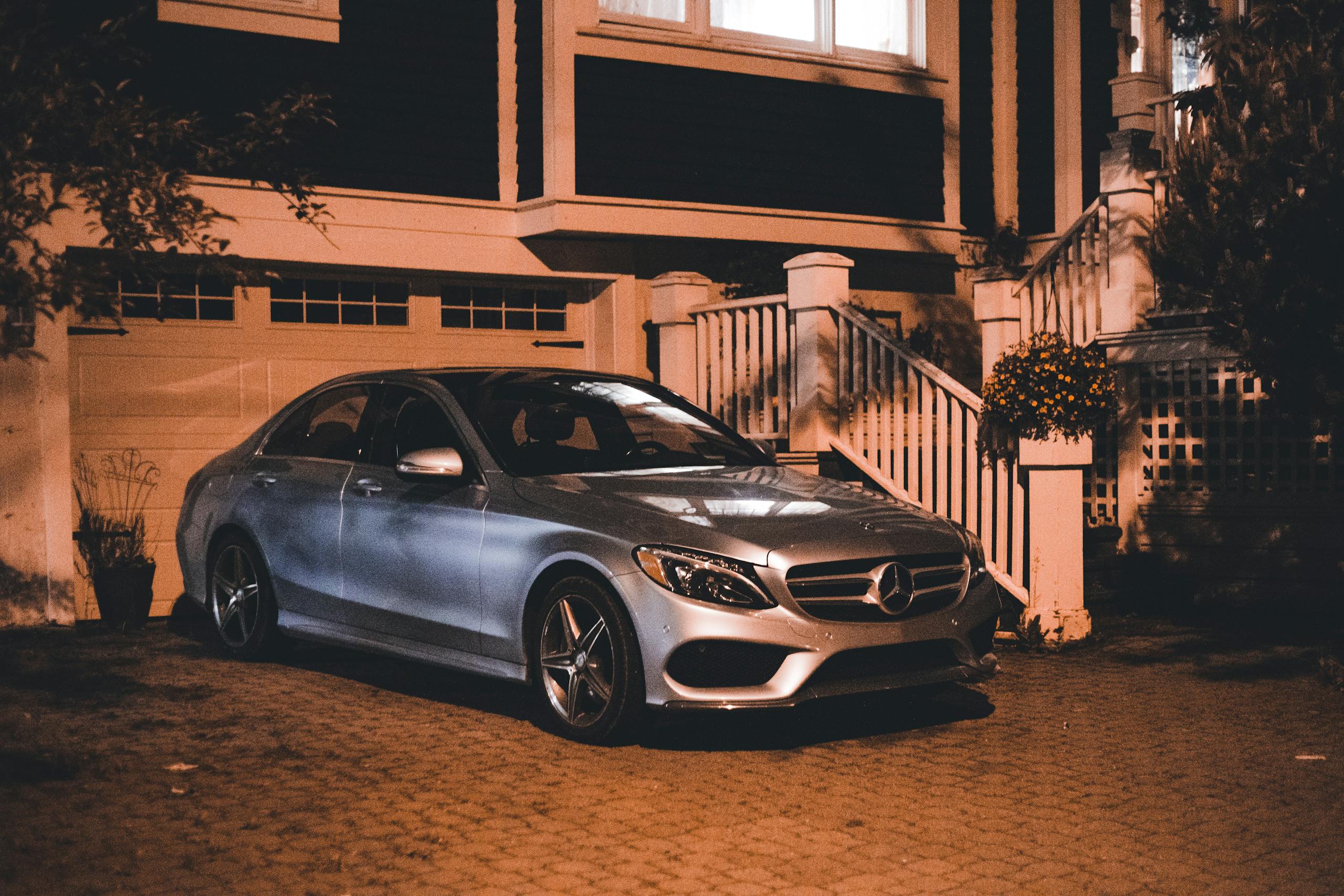 A silver luxury car is parked in a driveway at night, showcasing elegance and style.