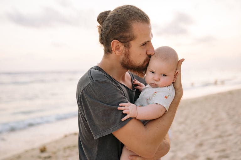A tender moment of a father holding his baby on a sandy beach during sunset.