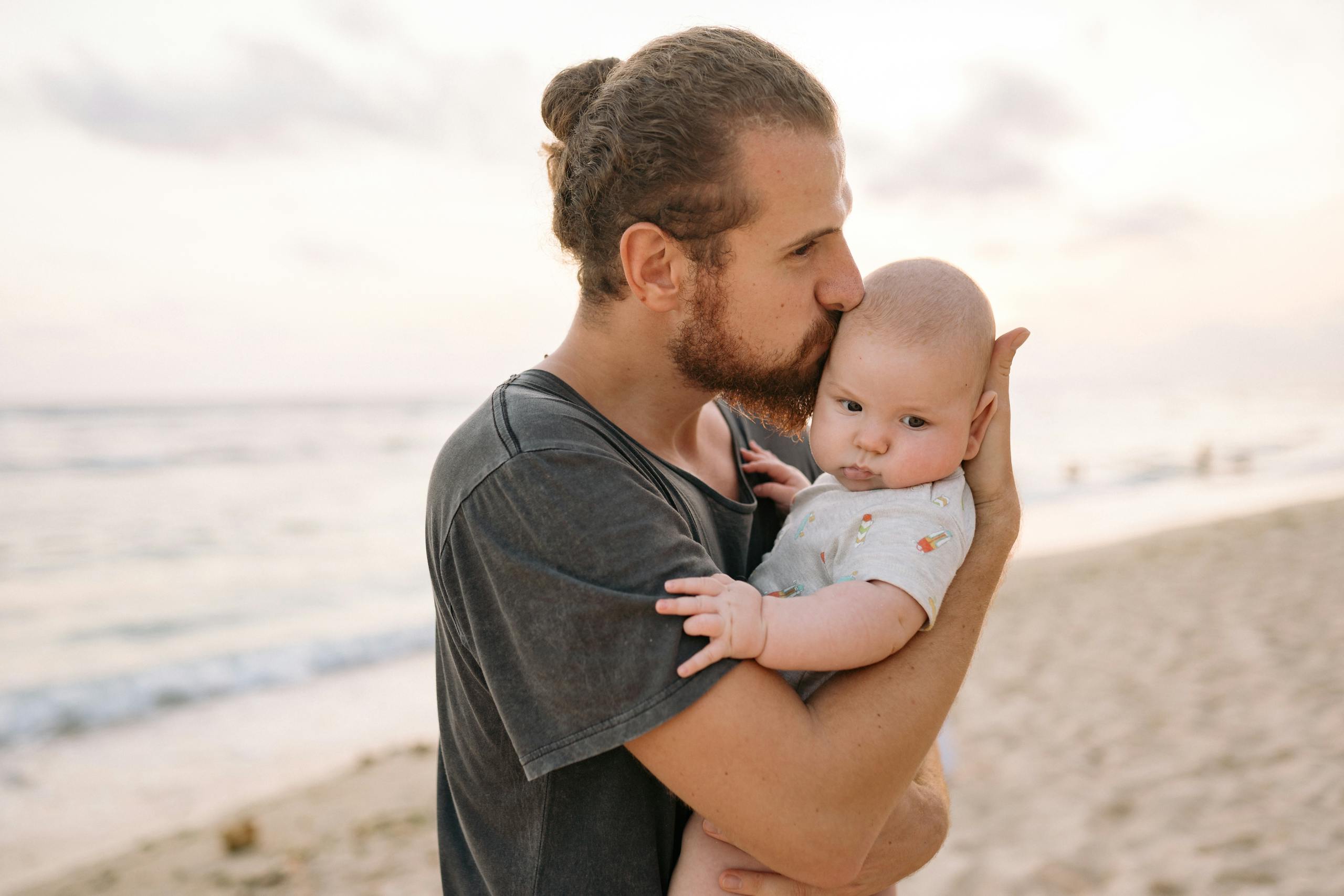 A tender moment of a father holding his baby on a sandy beach during sunset.