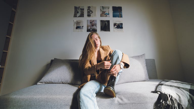 A thoughtful woman in a brown coat sitting on a couch with a casual and modern interior setting.