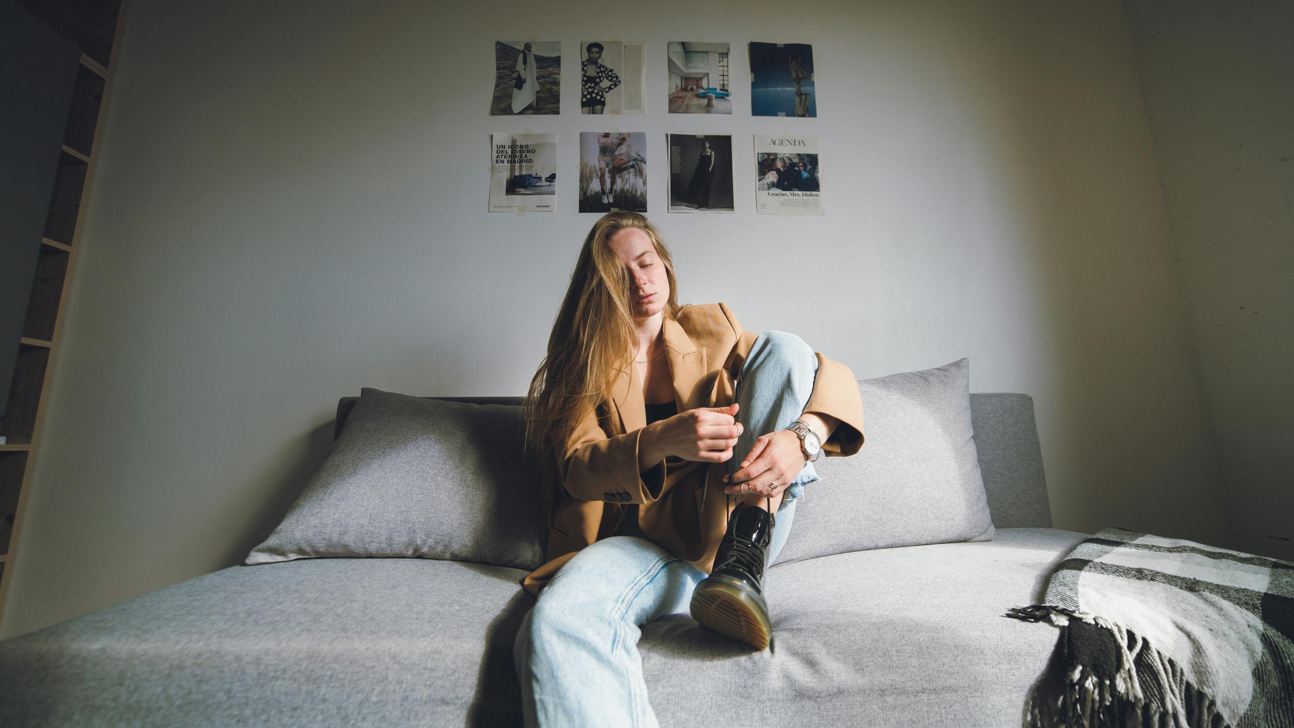 A thoughtful woman in a brown coat sitting on a couch with a casual and modern interior setting.