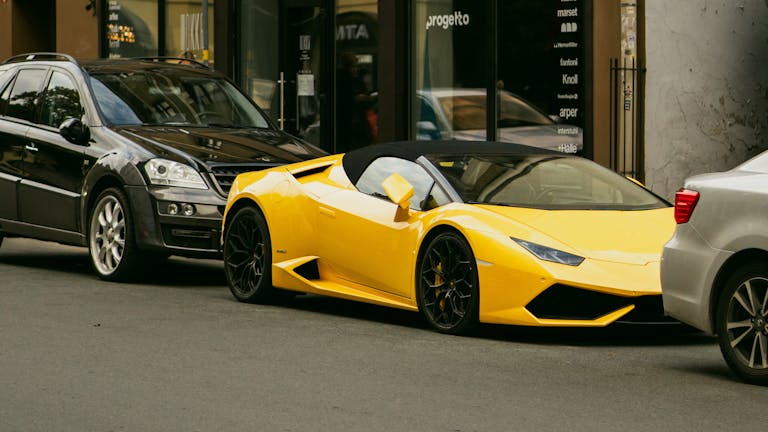 A vibrant yellow sports car parked between two other vehicles on a city street.