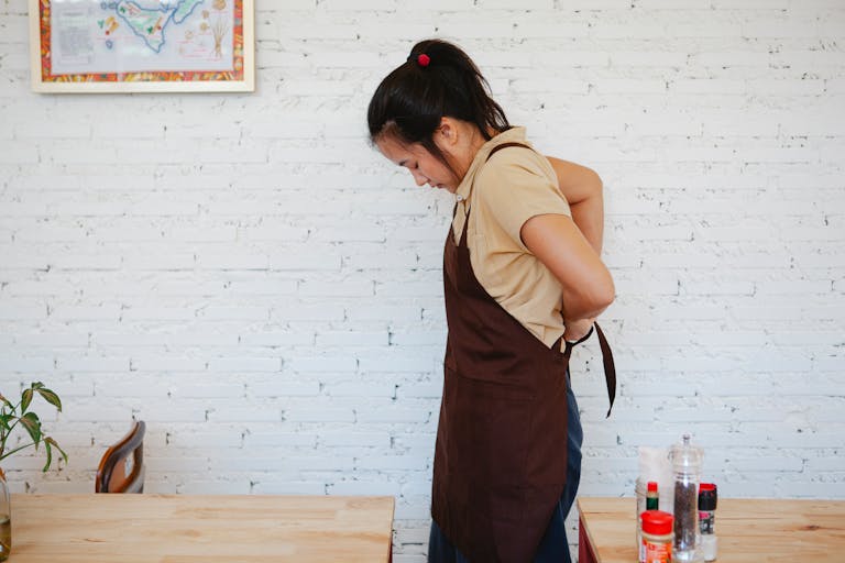 A waitress adjusts her apron inside a café with a white brick wall background.