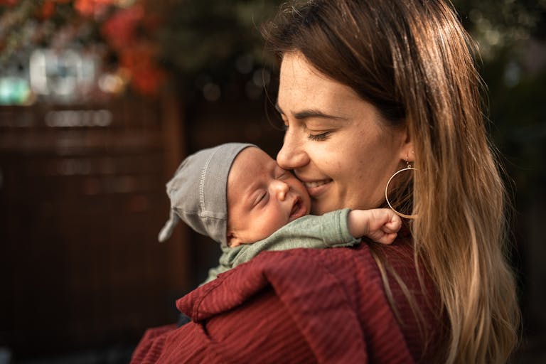 A warm embrace between a mother and her sleeping newborn baby outdoors.