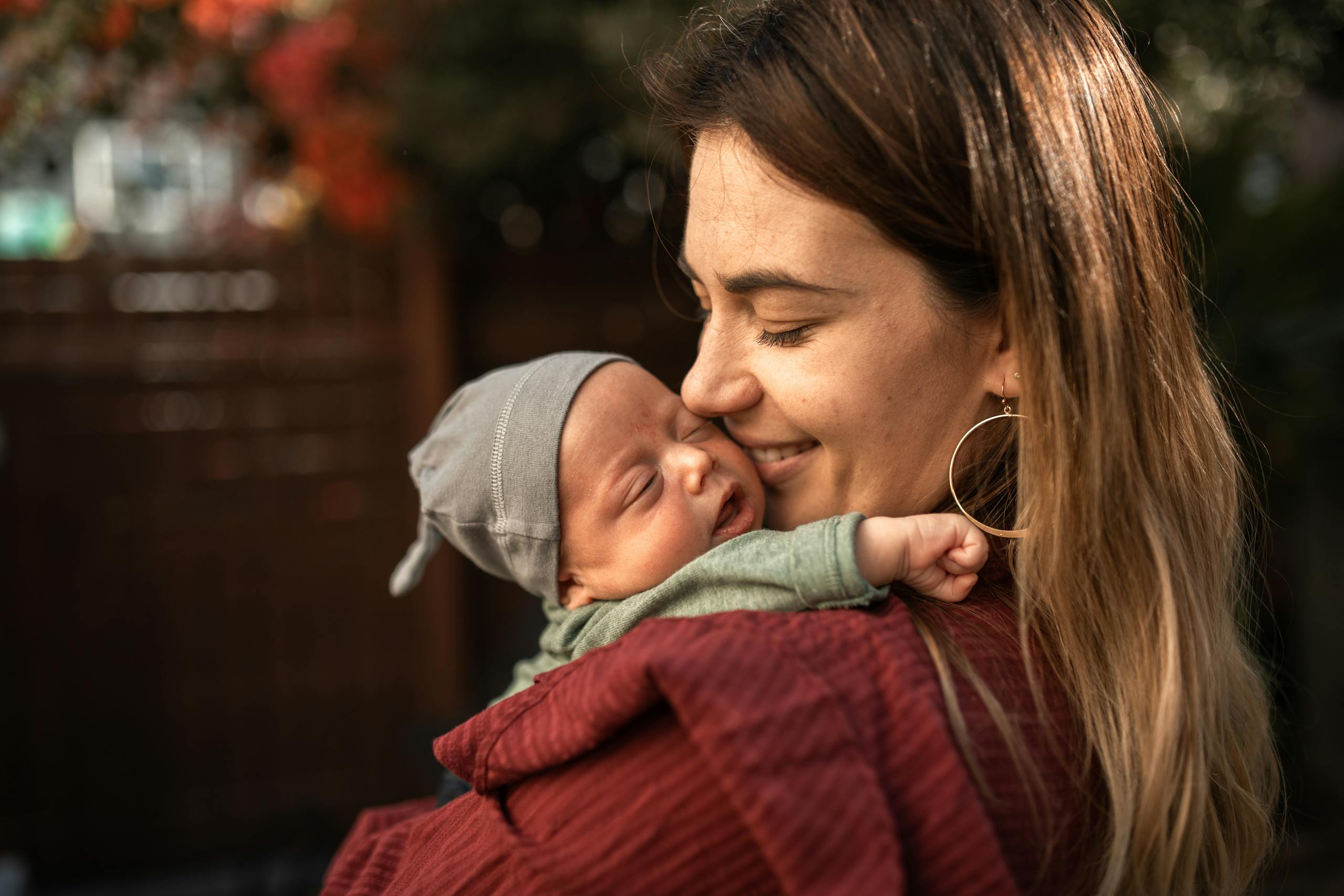 A warm embrace between a mother and her sleeping newborn baby outdoors.