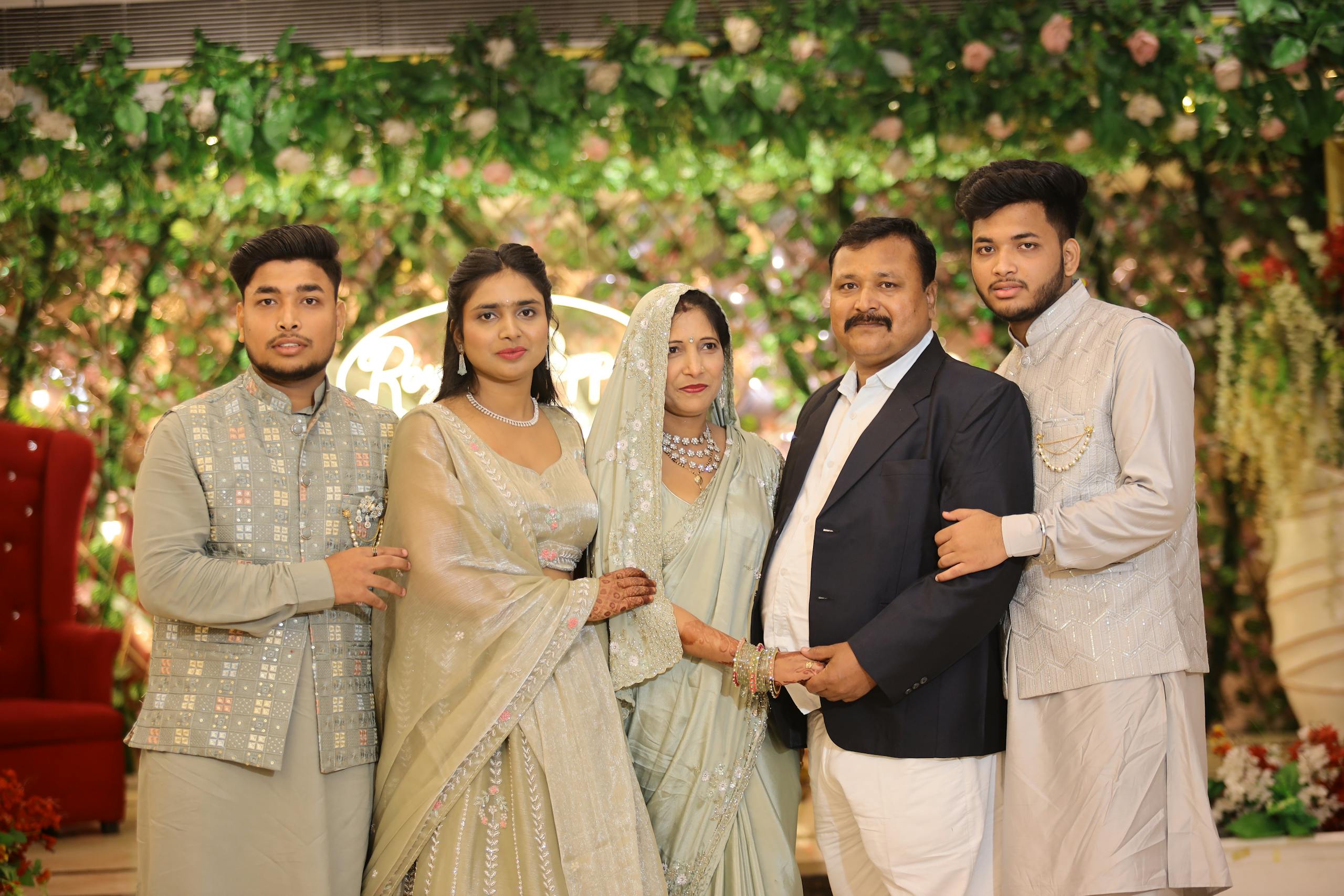 A well-dressed family poses together at a formal event against a floral backdrop.